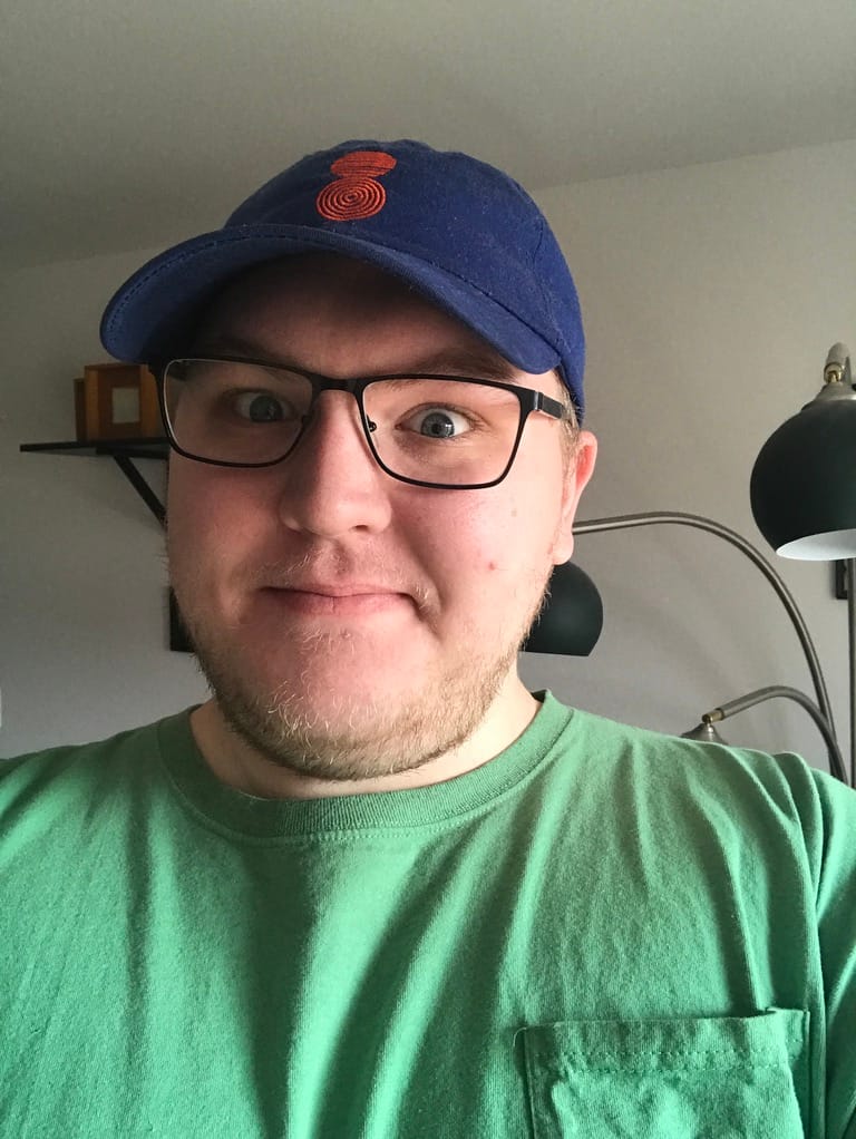 Jeff Perry wearing a green shirt and a blue hat smiling at the camera